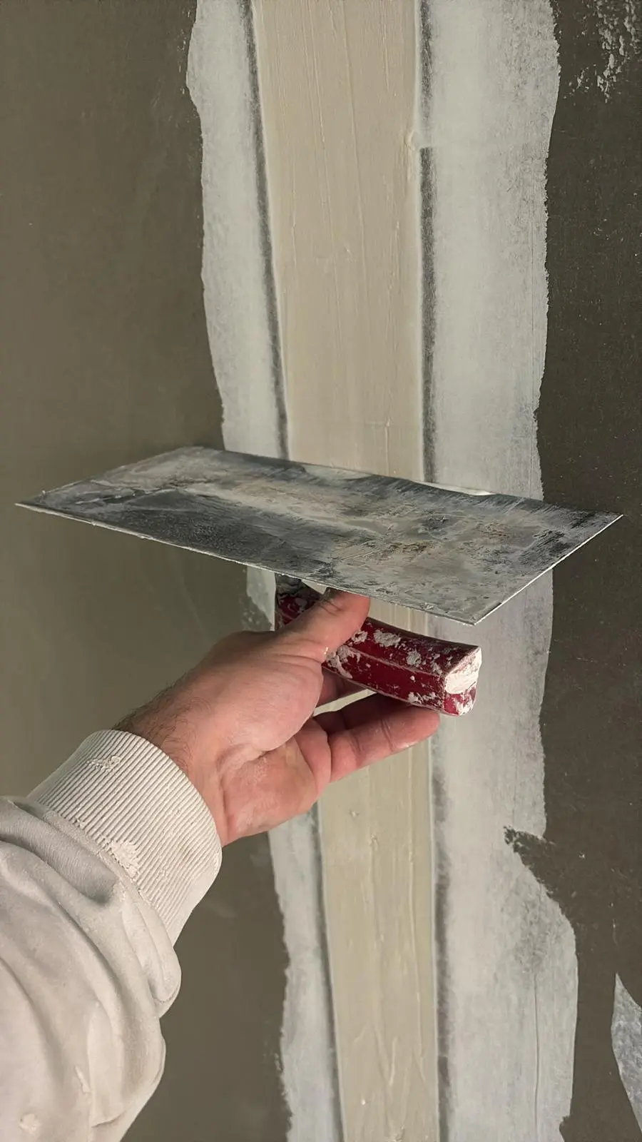 Hand mit Spachtel beim Glätten einer frisch verputzten Wand